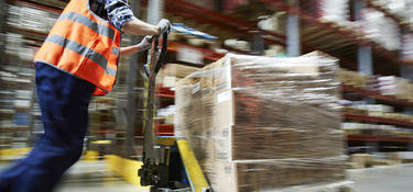 Worker pushing a pallet jack loaded with inventory inside a warehouse