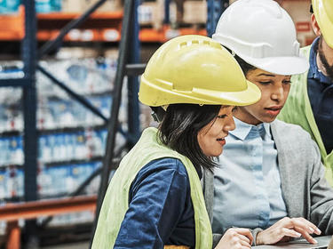 Team members look at a laptop screen inside a warehouse 